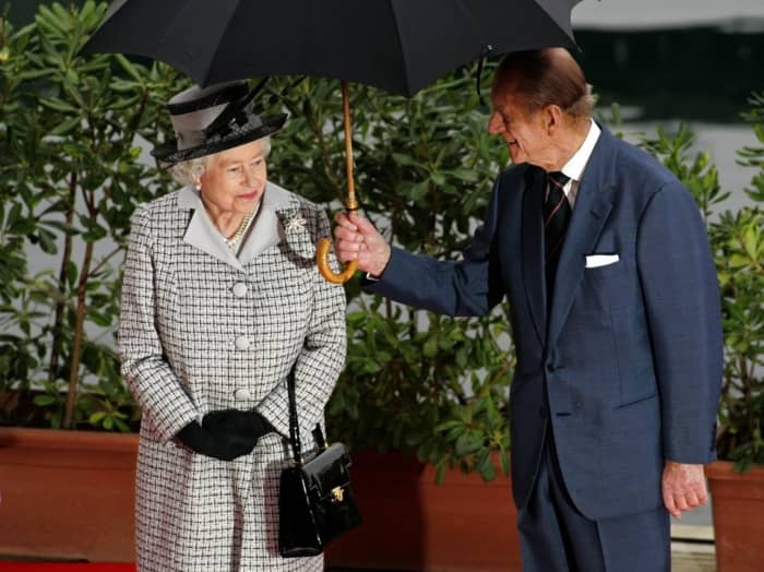 Принц Филипп держит зонтик для своей жены во время визита на Мальту.